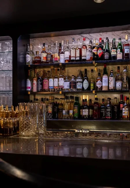 Fully stocked speakeasy bar shelves with premium liquor bottles.